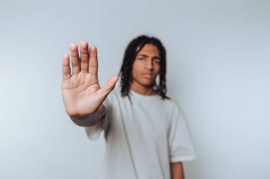 Genç bir adamın portresi avucunu dışa doğru ciddi bir ifadeyle kaldırıyor, ışık arkaplanındaki dur işaretini somutlaştırıyor.