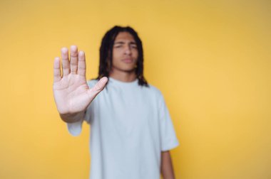 Genç adamın portresi sarı arka planda dur işareti olarak elini kaldırır.