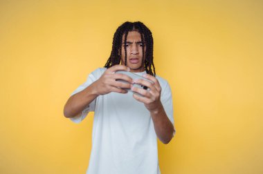 Akıllı telefonunu incelerken kafası karışmış genç bir adamın portresi sarı arka plandaki merakı vurguluyor