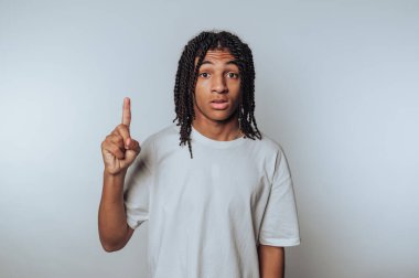 Genç bir bireyin portresi, hafif arkaplana odaklanmanın önemini sembolize eden düşünceli bir jestle parmağını kaldırır.