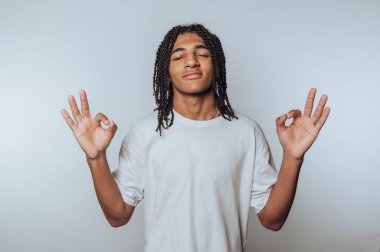 Genç bir adamın portresi meditasyon pozu, gözleri kapalı, sükuneti ve iç huzuru ışık arka planında ifade ediyor.