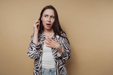 Zebra desenli tişörtlü endişeli genç bir kadının portresi sakin sarı arka plandaki bir telefon görüşmesinde endişe gösteriyor.