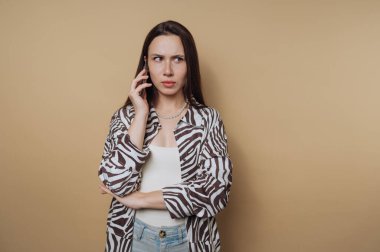 Endişeli genç bir kadının portresi telefonuna konuşuyor, sakin sarı arka planda şaşkınlık ifadesi sergiliyor.