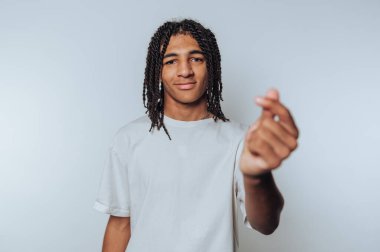 Genç adamın portresi, parmaklarıyla bir kalp şekli oluştururken kameraya şakacı bir şekilde bakar, ışık arka planında sıcaklık ve şefkat yayar.