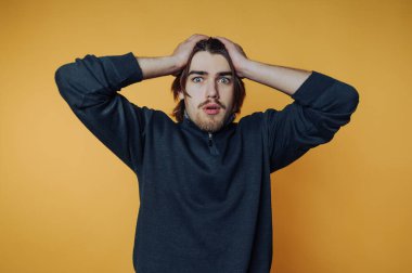 Genç bir adamın portresi, sarı arka plandaki şaşkınlık verici bir vücut diliyle duygularını vurgulayarak şok ve güvensizliği ifade eder.