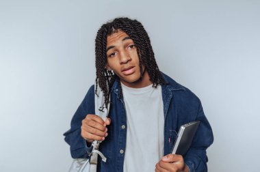 Genç adamın portresi sırt çantası ve dizüstü bilgisayarla gelişigüzel poz veriyor, hafif arka planda rahat ama kendinden emin bir görünüm sergiliyor.