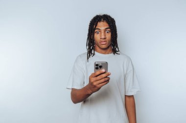 Genç bir adamın portresi telefonuna geniş gözlerle bakıyor, ışık arka planda bir tebligat ile ilgili şaşkınlık ve merakını dile getiriyor.