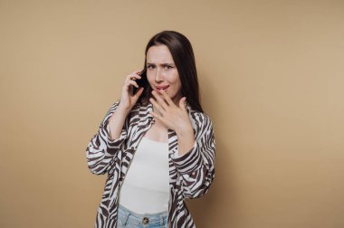 Zebra desenli tişörtlü endişeli genç bir kadının portresi sakin sarı arka plandaki bir telefon görüşmesinde endişe gösteriyor.