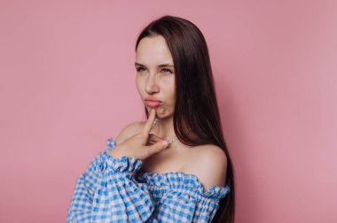 Pembe arka plan üzerinde düşünürken neşeli bir ifade sergileyen genç bir kadının portresi