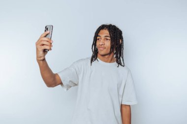 Genç adamın portresi mutlu bir şekilde arka planda akıllı telefonuyla selfie çekiyor.