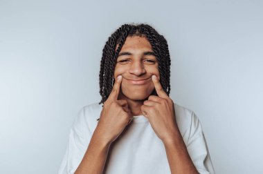 Genç adamın portresi açık arkaplanda şakacı bir şekilde yanaklarını gösterirken geniş bir gülümseme sergiliyor.