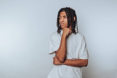 Genç bir adamın portresi, eli çenesinde düşünceli bir şekilde durur. Hafif arka planda merak ve yansıma yayar.