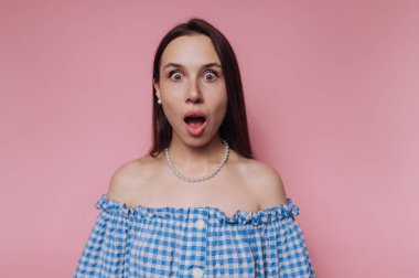 Geniş gözlü ve ağzı açık genç bir kadının portresi, pembe arka planda şaşkınlığını ifade ediyor.