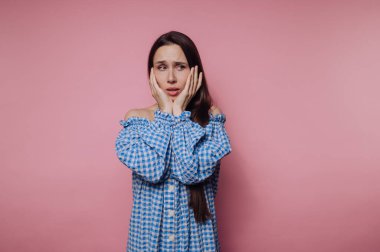 Genç bir kadının portresi pembe arka planda yüzüne dokunurken endişe ve endişe ifade eder.