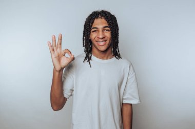 Rastalı genç adamın portresi gülümsüyor ve ışık arka planında pozitiflik ve neşe gösteren bir işaret veriyor.