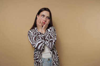 Düşünceli genç bir kadının portresi, sakin sarı arka planda düşünceli bir ruh halini yansıtan elleri üzerinde dinleniyor.