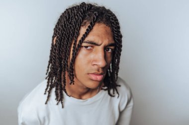 Rastalı genç adamın portresi kameraya yoğun bir şekilde bakıyor, ışık arkaplanı üzerinde bir anlık tefekkür görüntüsü yakalıyor.