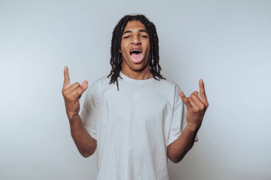 Genç bir adamın portresi bir kaya jesti sergiliyor elleriyle ve dilini dışarı çıkarıyor, ışık arka planında gençlik enerjisi ve eğlenceyi somutlaştırıyor.