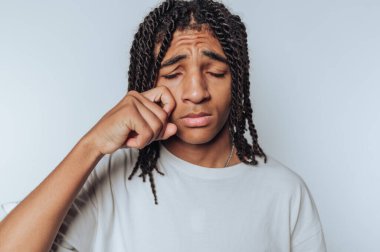 Genç bir adamın portresi göz yaşlarını bir anlık kırılganlıkla siler, hafif arka planda derin duyguları yansıtır.