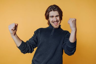 Genç adamın portresi, sarı arka planda mutluluk ve pozitiflik saçan büyük bir gülümseme ve yumruklarla kutluyor.