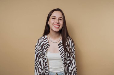 Zebra desenli giyinmiş genç bir kadının portresi parlak bir gülümseme, durgun sarı arka planda neşe ve pozitiflik saçar.