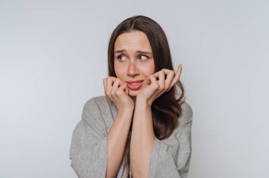 Hafif arka planda tırnaklarını yerken endişeli görünen genç bir kadının portresi