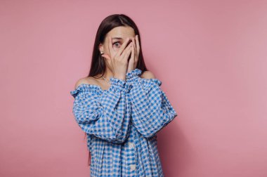 Genç bir kadının portresi ellerini şakaya vurarak yüzünü gizliyor. Pembe arka planda şaşkınlığını ifade ediyor.