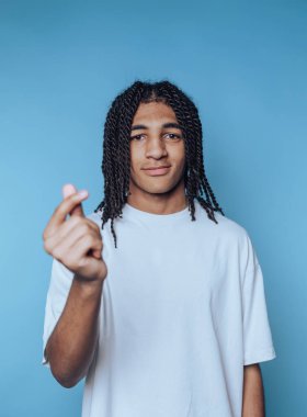 Genç bir adamın portresi mavi arka planda samimiyet ve dostluk saçan elleriyle bir kalp hareketi yapıyor.