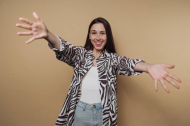 Genç ve neşeli kadının portresi kollarını geniş bir gülümsemeyle açıyor, sakin sarı arka planda heyecan ve hoş geldin enerjisi sergiliyor.