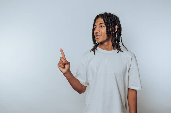 портрет молодого человека с плетеными волосами уверенно жестикулирует вверх, улыбаясь, демонстрируя энтузиазм на светлом фоне