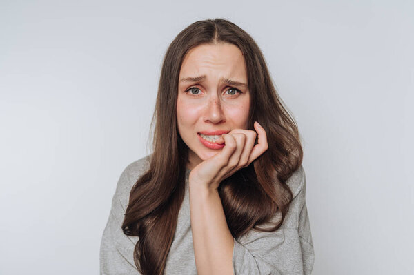 portrait of young woman bites her nail, showcasing anxiety and worry on light background