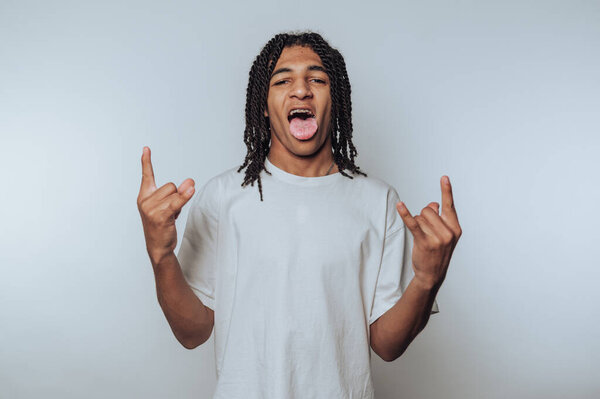 Портрет молодого человека показывает жест камня руками и высовывает язык, олицетворяя веселье и юную энергию на светлом фоне.