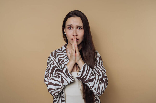 portrait of young concerned woman clasps her hands together thoughtfully, conveying a moment of introspection and vulnerability on calm yellow background