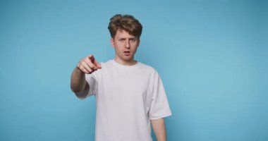 Kendine güveni olan genç bir adamın göz teması kurduğu ve mavi arka plandaki izleyiciyi neşeyle işaret ettiği görüntüler.