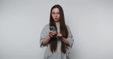 Akıllı telefonuyla etkileşime girerken gülümseyen genç bir kadının görüntüleri ışık arka planında neşe saçıyor.