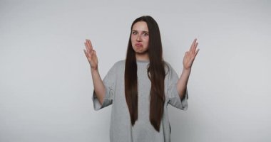 Gri elbiseli, kafası karışmış genç bir kadının elleri açık arka planda inançsızlık içinde büyük bir şey gösterdiği görüntüler.