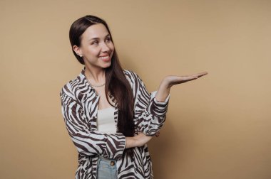 Uzun siyah saçlı bir kadın şık çizgili bir gömlek giyer ve eliyle işaret ederken gülümser. Sıcak arka plan bu ana neşe katıyor..