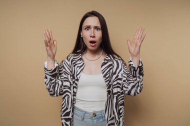 Genç bir kadın ağzı açık ve elleri havada şaşkınlık bakışları sergiliyor. Çizgili bir gömlek giyiyor ve beklenmedik bir habere ya da şok edici bir olaya tepki veriyor gibi görünüyor..