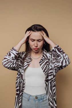 Genç bir kadın sıkıntılı bir ifadeyle ayakta duruyor, bir hüsran jesti olarak başını tutuyor. Şık bir zebra desenli ceket giyiyor ve oldukça endişeli görünüyor..