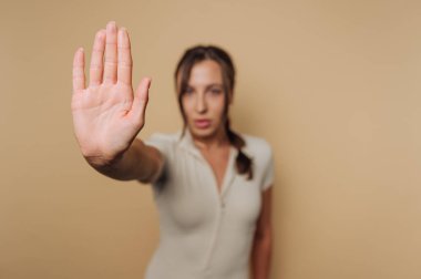 Bir kadın elini kaldırmış, sessizlik ya da duraksama işareti veriyor. Kendine güvenen bir ifadesi var. Minimalist bir ortamda otorite ve sakinlik yayıyor..