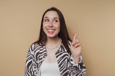 Tarafsız bir arkaplanda duran genç bir kadın ışıl ışıl gülümsüyor. Parmaklarını çapraz yapıyor, umut ve beklenti duygusu taşıyor, şık bir zebra desenli bluz giyiyor..