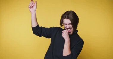 Siyah kazaklı adam sevinçle dans ediyor sarı arka planda.