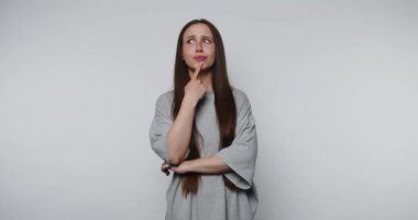 Gri tişörtlü genç bir kadın çenesinde parmak ile düşünüyor..