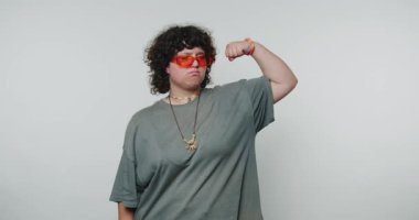 Kırmızı güneş gözlüğü takan ve kaslarını esneten gri tişörtlü biri..