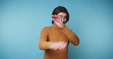 Turuncu kazaklı bir adam mavi arka planda kollarını kavuşturuyor..