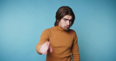 Kahverengi kazaklı genç adam mavi arka planda kameraya bakıyor..