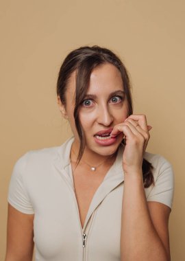 Bej arka planda endişeli bir ifadeyle tırnaklarını yiyen bir kadın..