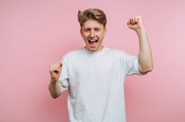 Genç adam yumrukları havada, pembe arka planda kutluyor.