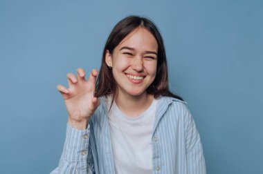 Gülümseyen kadın, mavi arka planda bir pençe hareketi yapıyor..