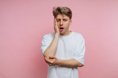 Beyaz tişörtlü genç adam pembe arka plana şaşırmış görünüyor..